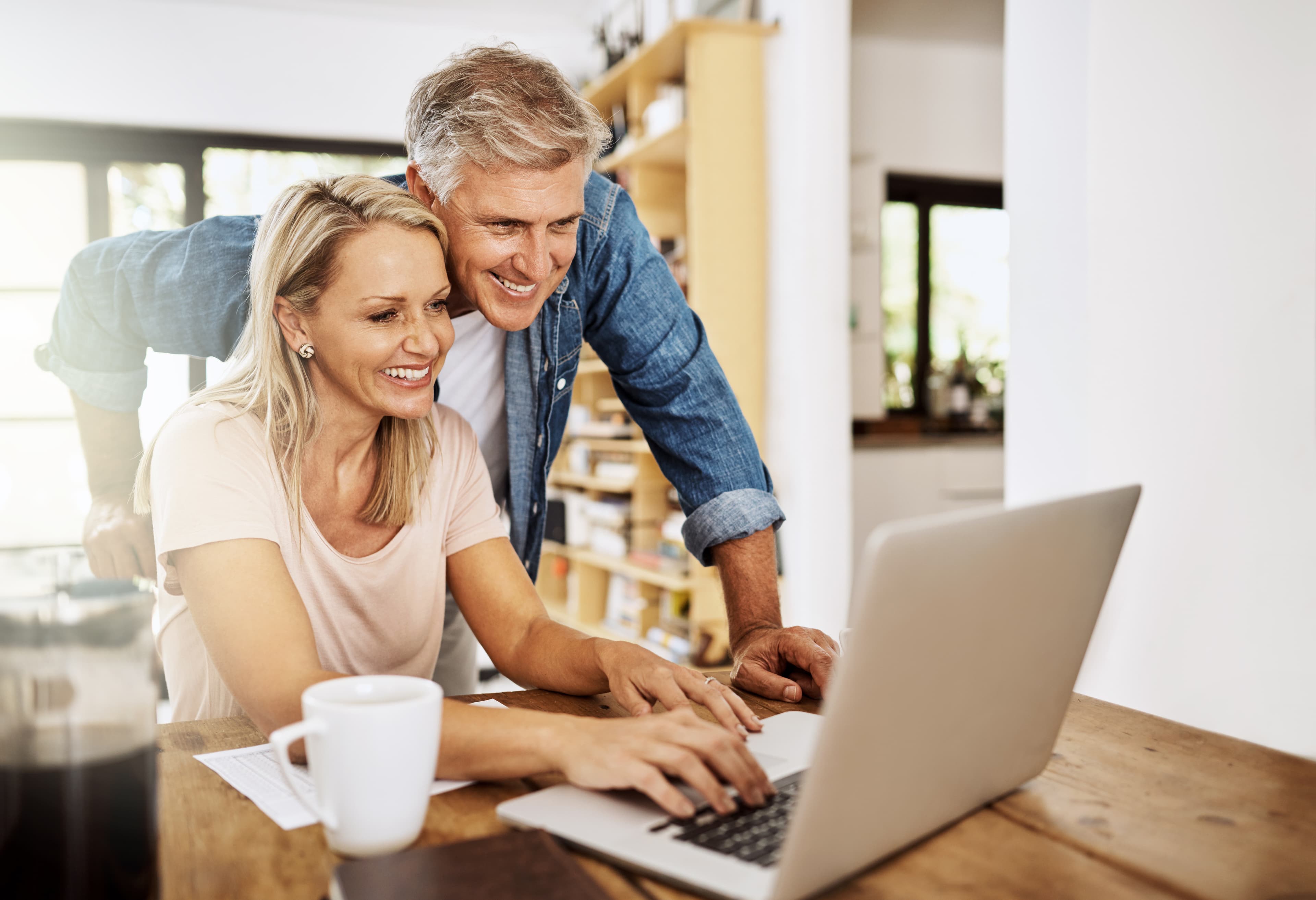 A couple at home smiling as they look at a laptop together at the kitchen table